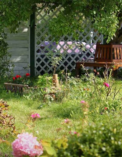 Garten mit Sitzbereich und blühenden Pflanzen auf dem Grundstück der Ferienwohnungen - Entspannen unter Pflaumenbäumen